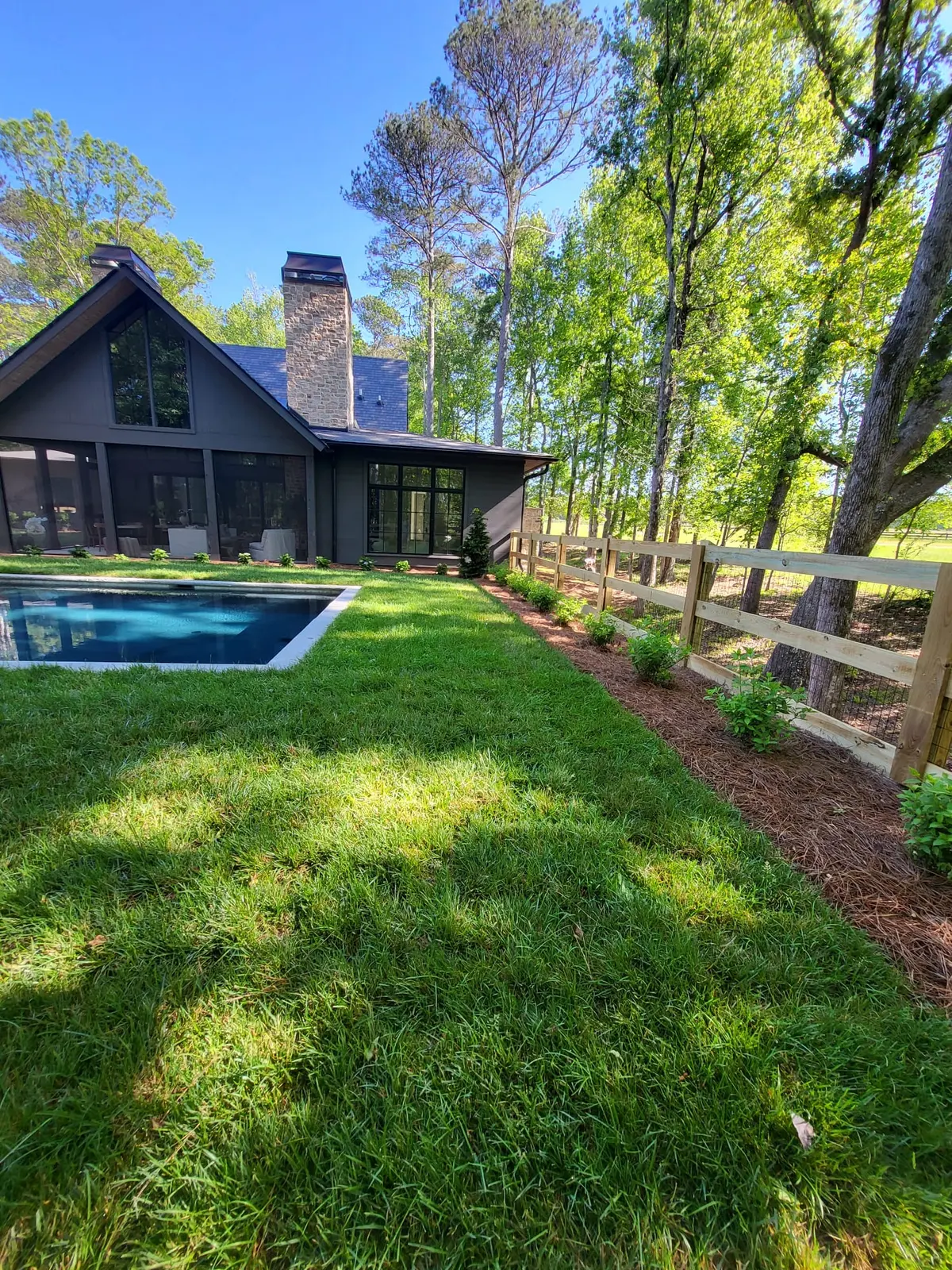 Fresh sod lawn and pine straw beds running to a pool beside a black-clad farmhouse