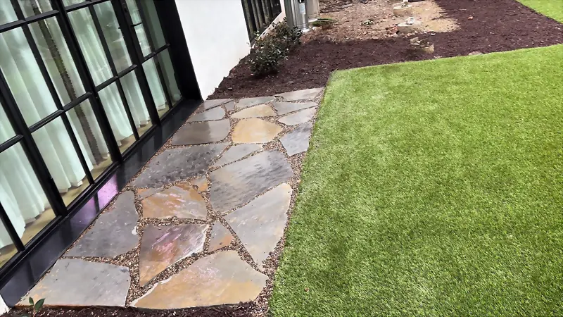 Irregular flagstone landing meeting a manicured turf lawn at a modern home