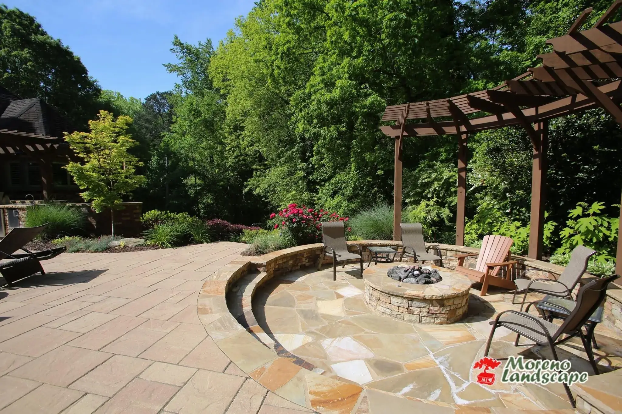Cedar pergola over a flagstone terrace with a stacked-stone fire pit, curved seat wall, and layered planting beds