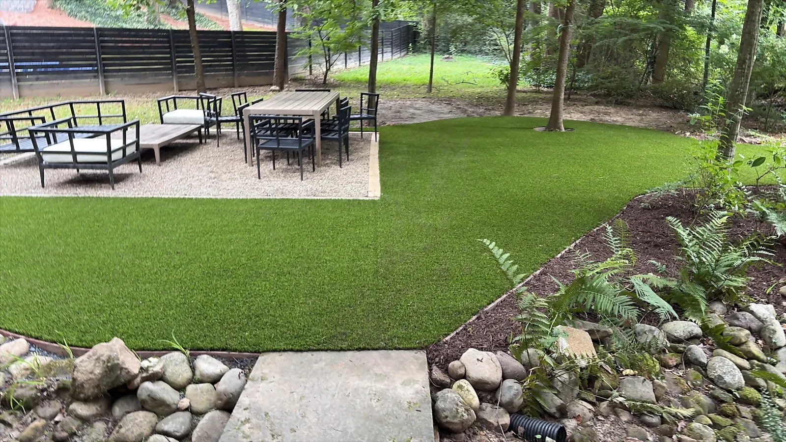 Turf lawn meeting a gravel terrace with outdoor dining and lounge seating under mature trees