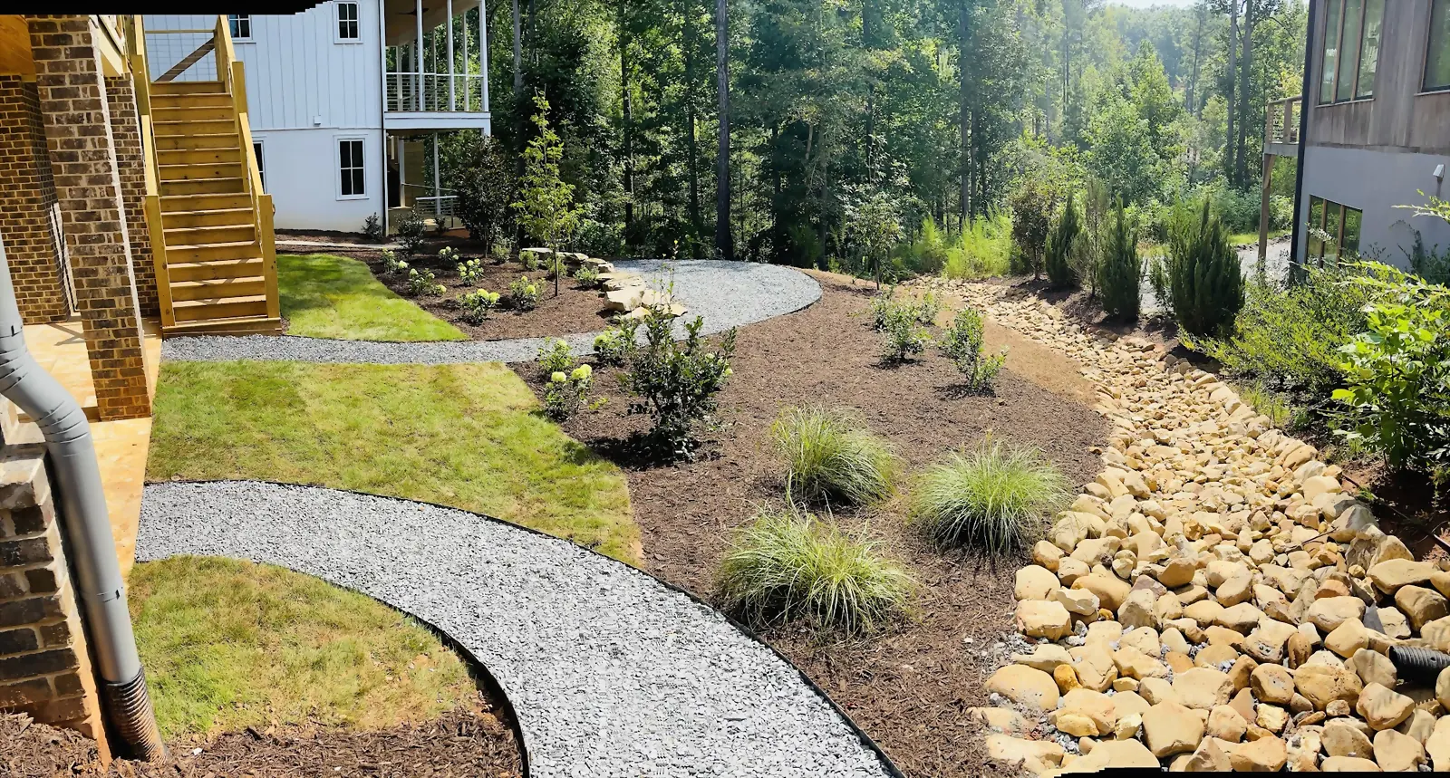 A finished back garden with lawn, a gravel path, a stone drainage bed and new planting running back toward the house