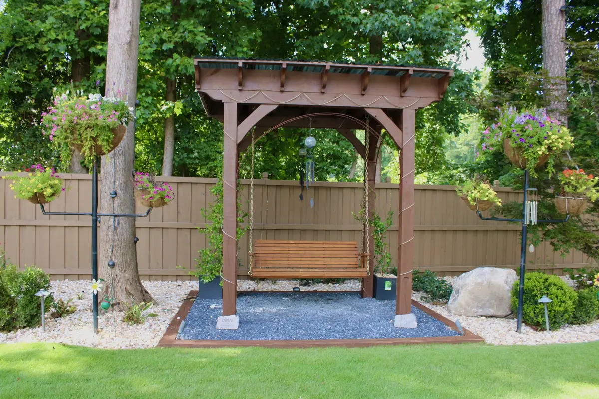 Timber pergola over a porch swing, set on gravel with stone edging and hanging baskets