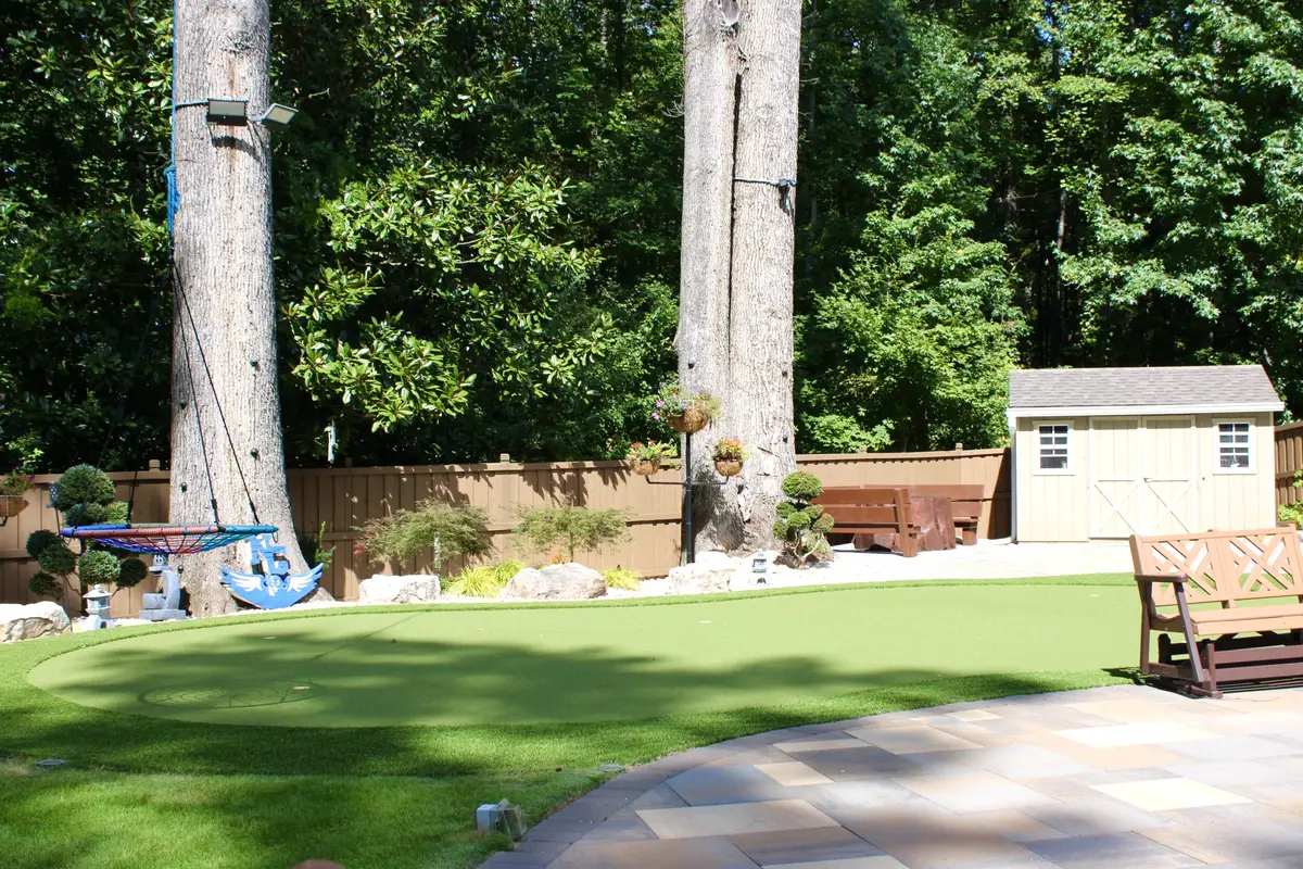 Synthetic putting green curving through a back garden beside a paver terrace