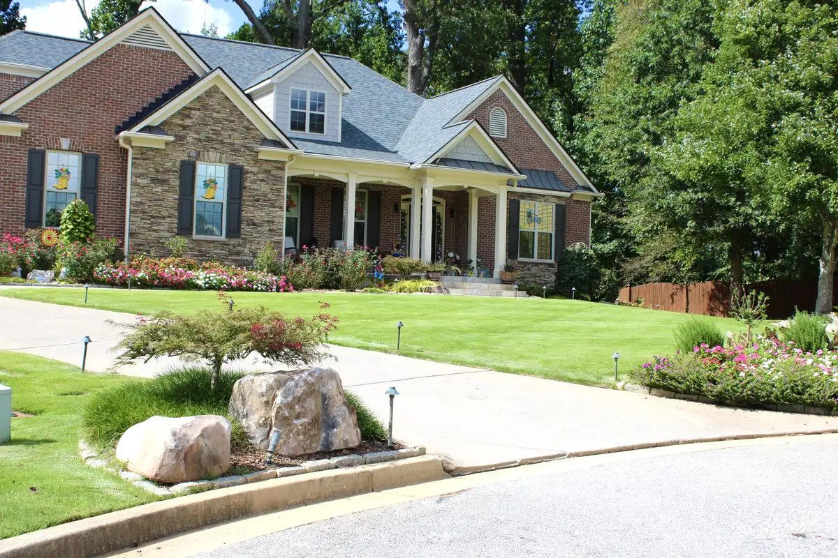 Stone and brick home entry with boulder-edged beds and seasonal color along the drive
