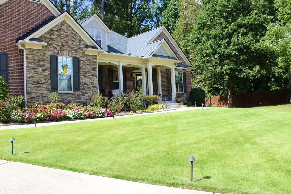 Striped mown lawn running up to a stone house with flower borders along the foundation