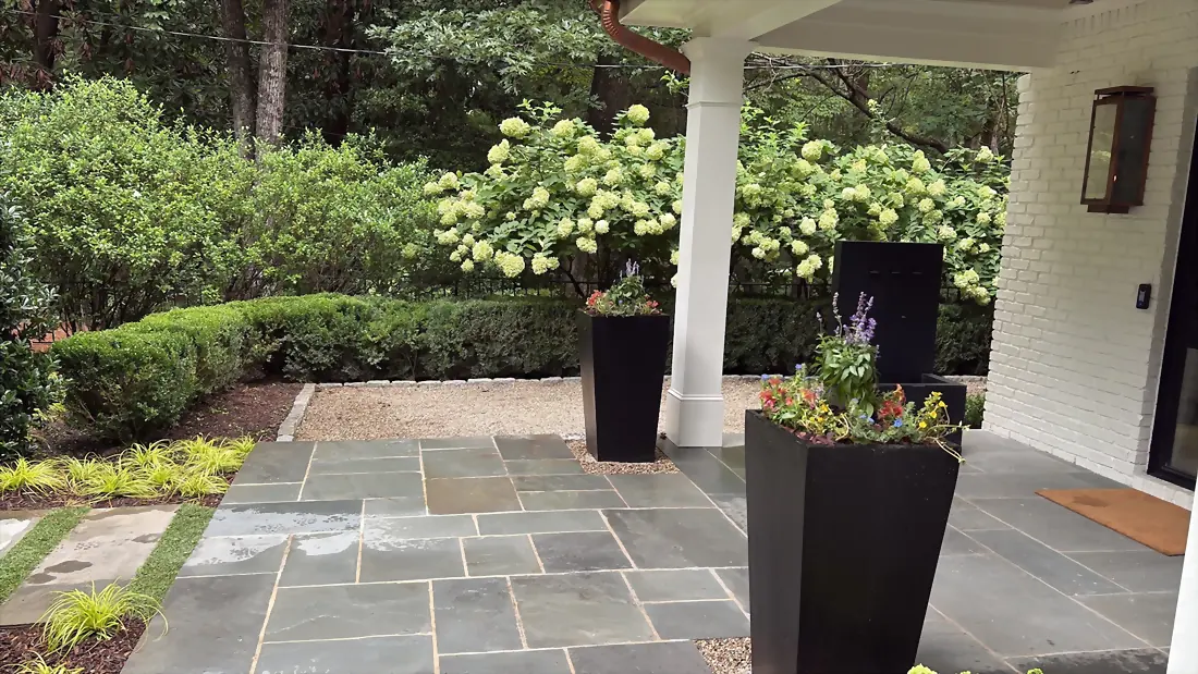 Bluestone patio with tall dark planters and hydrangeas beside a covered walkway