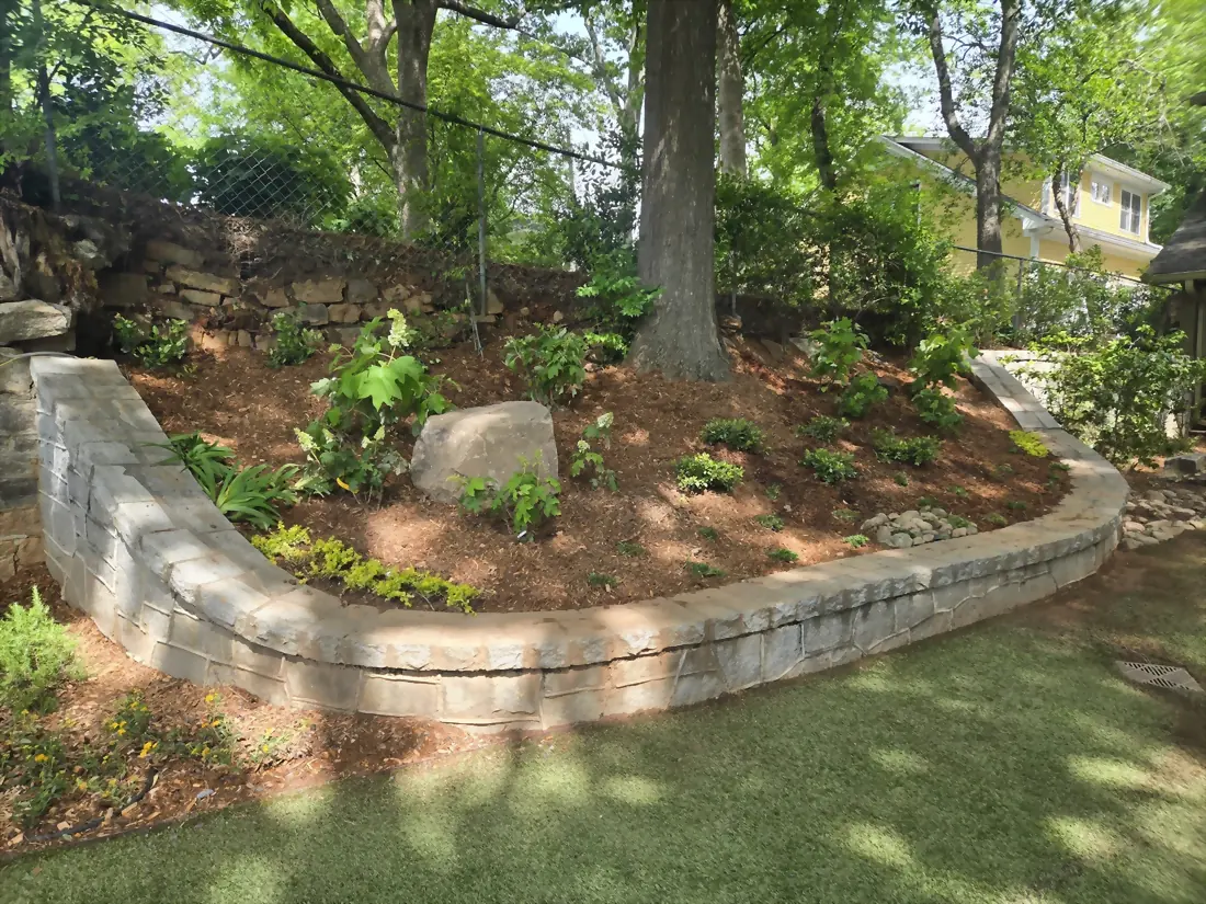 Curved stacked-stone retaining wall around a mulched tree bed