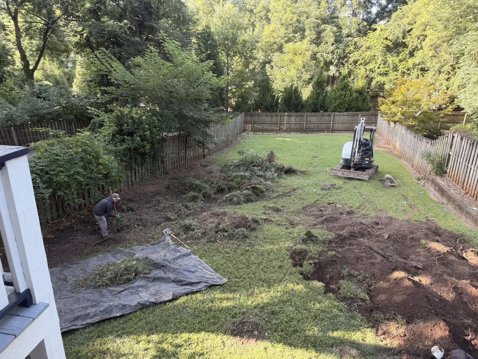 Crew clearing a back yard with a compact excavator and debris tarps