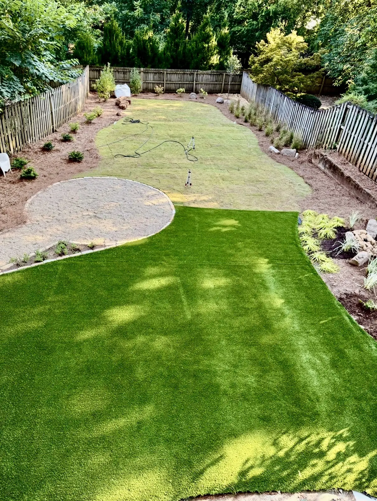 Fresh sod laid behind a finished artificial turf lawn, sprinklers still running