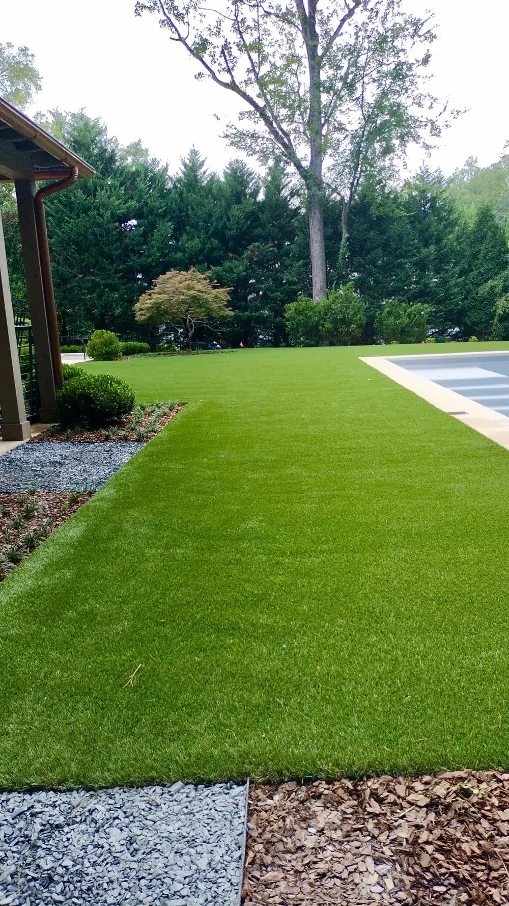 Artificial turf lawn running the length of a pool, edged in gravel and mulch beds