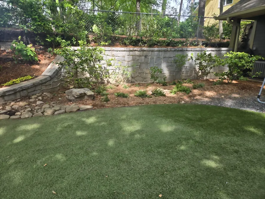 Turf lawn set below a stacked stone wall and planted bank